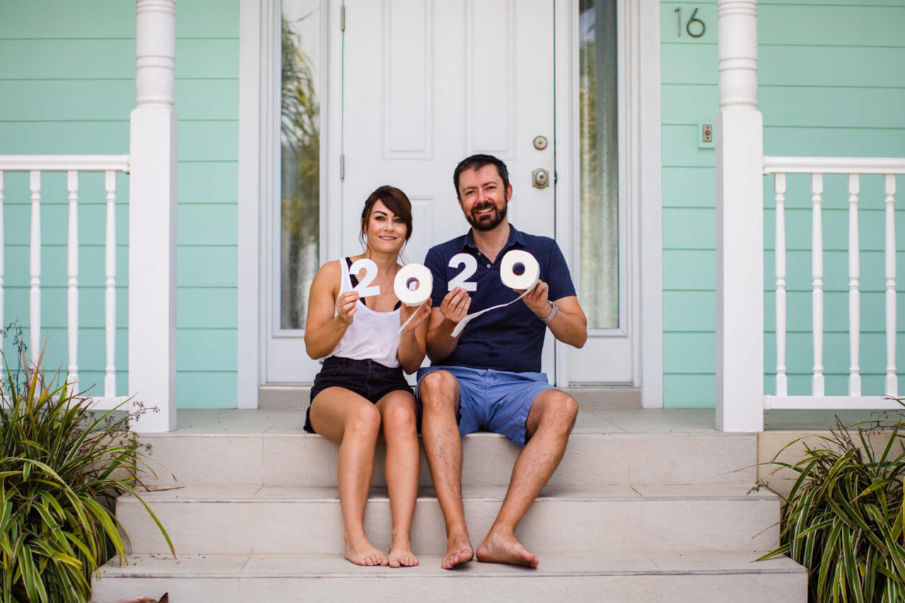 Wanita dan pria duduk di teras depan rumah bercat biru muda sambil memegang tissue bertuliskan 2020